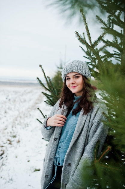 Retrato de mujer gentil en abrigo gris y sombrero contra el árbol de Navidad al aire libre.