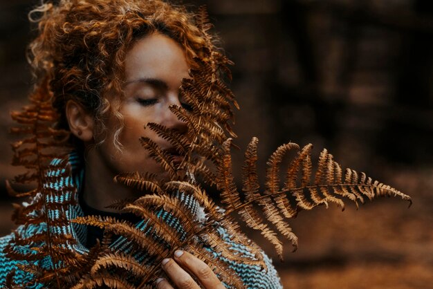 Retrato de mujer con gran hoja tropical seca marrón y fondo de naturaleza oscura Actividad de ocio al aire libre y sentir conexión con el bosque Medio ambiente estilo de vida Gente en el bosque Ojos cerrados