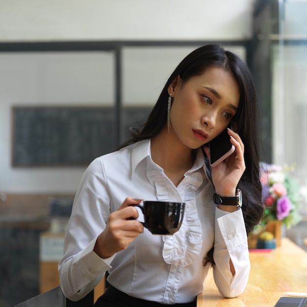 Retrato de mujer hablando por teléfono mientras bebe café en cafa