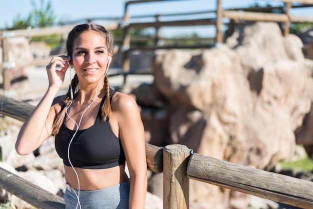 Retrato de una mujer haciendo deporte descansando al aire libre sonriendo y escuchando música