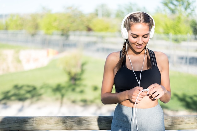 Retrato de una mujer haciendo deporte descansando al aire libre sonriendo y escuchando música