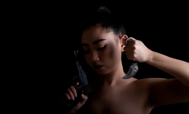 Retrato de mujer hermosa de Asia con una mano sosteniendo una pistola y un cuchillo karambit en el fondo negro