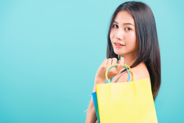 Retrato mujer hermosa asiática feliz sonriendo sosteniendo bolsas de compras sobre fondo azul, con espacio de copia de texto