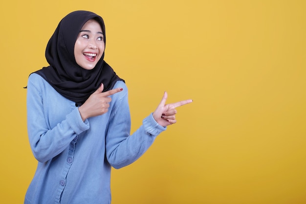 Retrato de mujer hermosa asiática con hijab negro, mira feliz expresión apuntando con el dedo índice