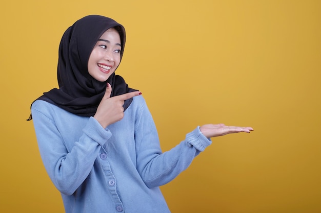 Retrato de mujer hermosa asiática con hijab negro, mira feliz expresión apuntando y mostrando con el dedo índice