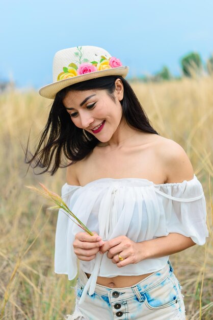 Retrato de mujer hermosa asiática sintiendo un sombrero fresco en la mano en el denim de campo con bota marrón