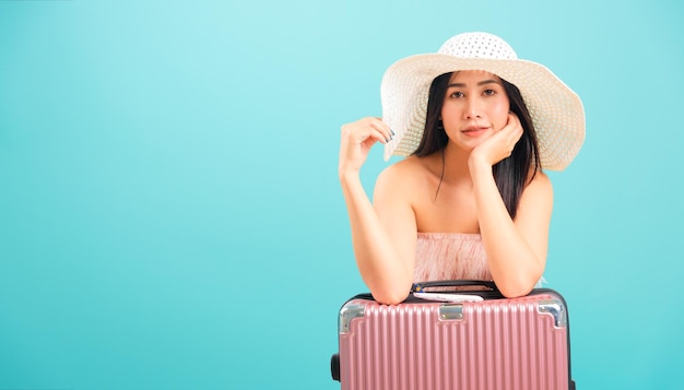 Retrato mujer hermosa asiática con sombrero sentada con bolsa de viaje los fines de semana sobre fondo azul, con espacio para copiar texto