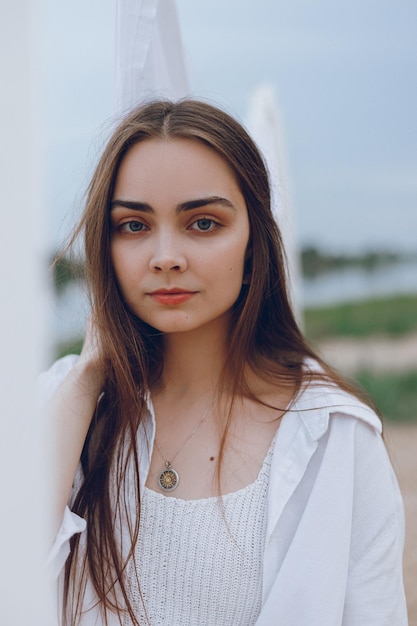 Retrato de mujer hermosa con cabello castaño en lino blanco de pie cerca de ropa seca al aire libre