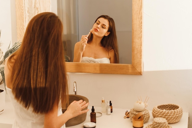 Retrato de una mujer hermosa envuelta en una toalla blanca para masajear su rostro con un rodillo de bola en forma de Y Concepto de cosmética natural alisado de arrugas