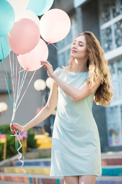 Retrato de mujer hermosa feliz con globos multicolores volando en la ciudad