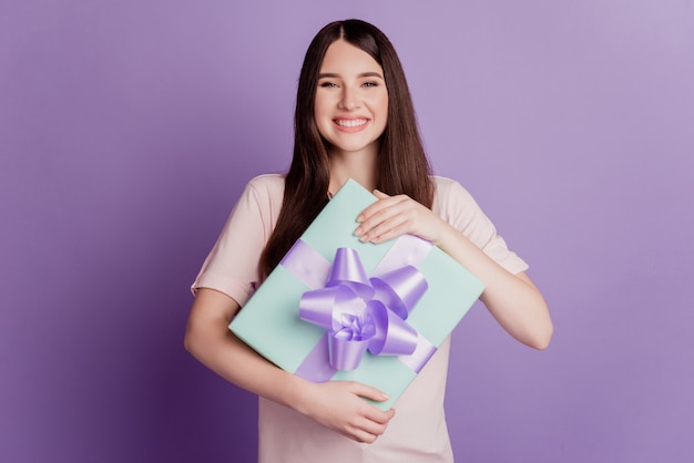 Retrato de mujer hermosa feliz mantenga presente regalo en pared púrpura
