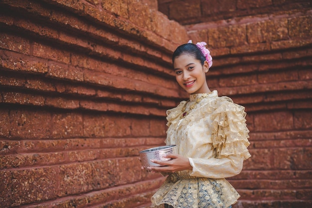 Retrato de una mujer hermosa en el festival Songkran con traje tradicional tailandés en el templo sosteniendo un tazón de agua y sonríe la cultura de Tailandia con el festival del agua