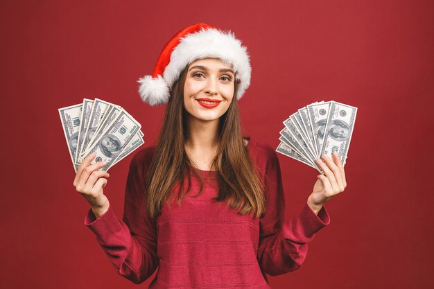 Retrato de mujer hermosa con gorro de Papá Noel y sosteniendo billetes de dólar