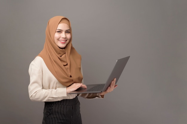 Retrato de mujer hermosa con hijab está sosteniendo la computadora portátil en gris