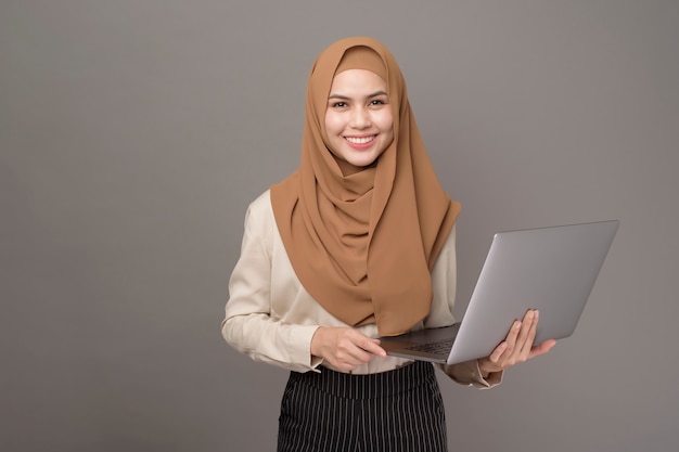 Retrato de mujer hermosa con hijab está sosteniendo la computadora portátil en gris