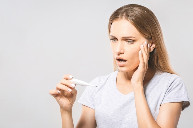 Retrato de una mujer hermosa joven preocupada que controla su temperatura. Fondo blanco, gripe.