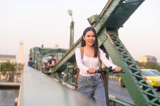 Retrato de mujer hermosa joven con un scooter eléctrico sobre el puente en el fondo de la ciudad moderna