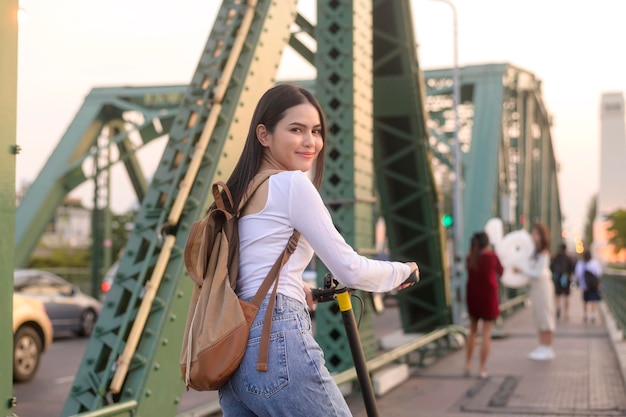 Retrato de mujer hermosa joven con un scooter eléctrico sobre el puente en el fondo de la ciudad moderna