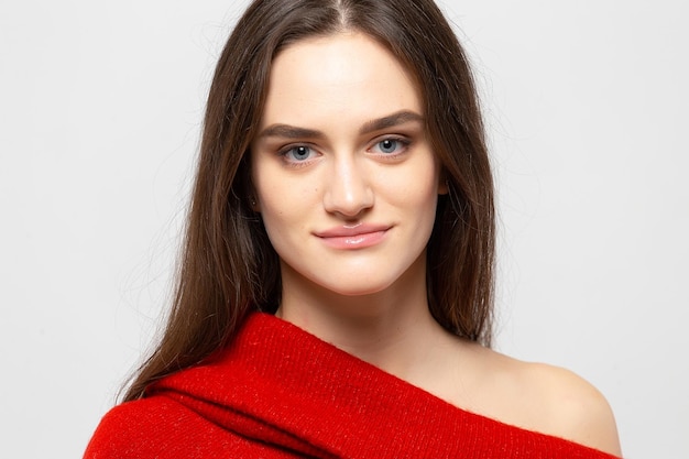 Retrato de una mujer hermosa joven con una sonrisa ligera vestida con un suéter rojo sobre un fondo gris claro