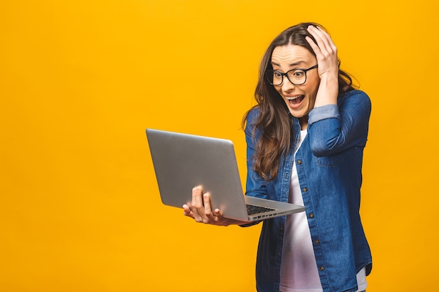 Retrato de una mujer hermosa joven sorprendida que sostiene la computadora portátil