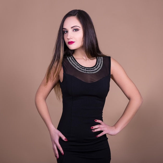 Retrato de mujer hermosa joven en vestido negro posando sobre fondo beige