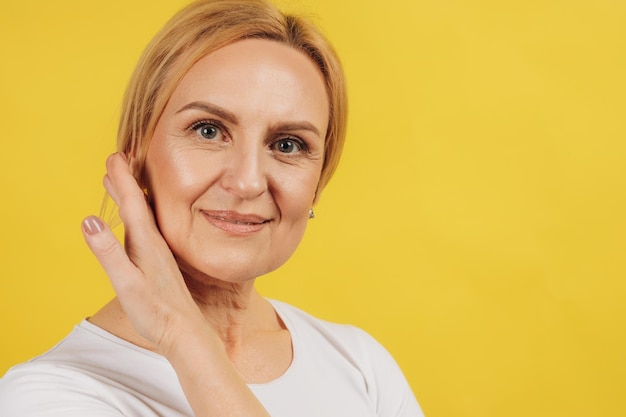 Retrato de mujer hermosa madura sosteniendo la mano cerca de la cara sobre fondo amarillo