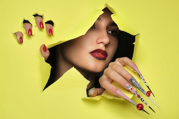 Retrato de una mujer hermosa con maquillaje artístico en estilo glamuroso, uñas largas creativas sobre un fondo amarillo Diseño de manicura Cara de belleza