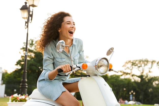 Retrato de mujer hermosa, montando en elegante moto por las calles de la ciudad