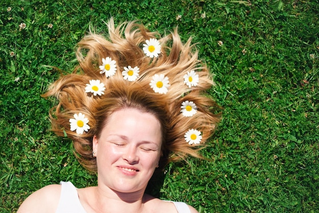 El retrato de una mujer hermosa con los ojos cerrados tirados en el campo con flores de manzanilla en el pelo