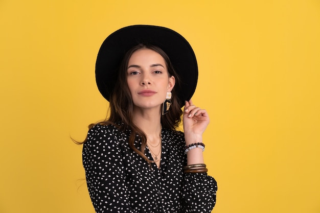 Retrato de mujer hermosa posando aislado en amarillo con vestido negro punteado y sombrero negro