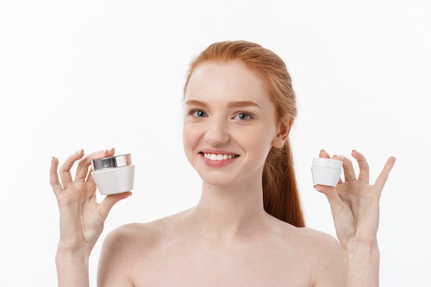 Retrato de la mujer hermosa que sonríe mientras que toma un poco de crema facial aislada en el fondo blanco con el espacio de la copia.