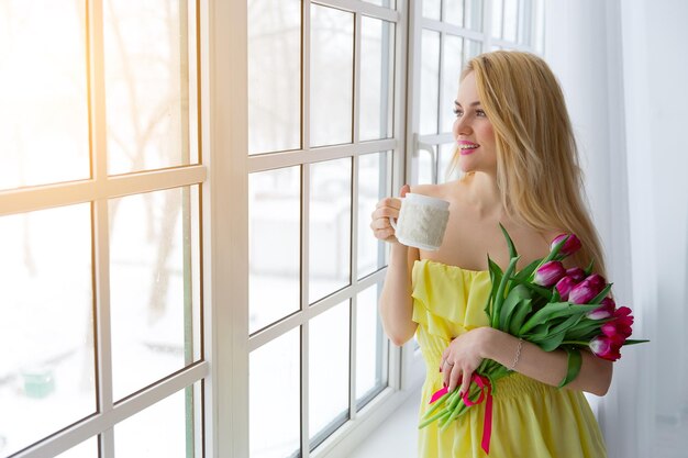 Retrato de mujer hermosa con ramo de tulipanes y taza de té luz del sol