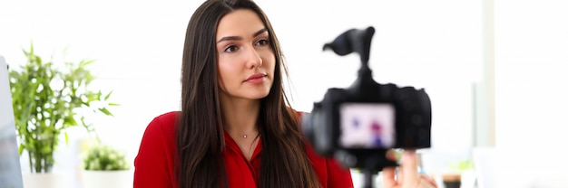 Foto retrato de mujer hermosa en rojo dando entrevista en la oficina de la empresa. inteligente morena empleada hablando por cámara. trabajador con portapapeles. concepto de reunión de negocios