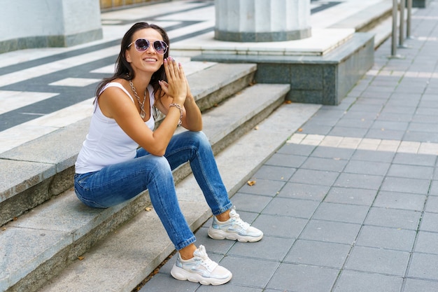 Retrato de mujer hermosa en ropa casual y gafas de sol sentado en las escaleras en la ciudad con estilo y ...