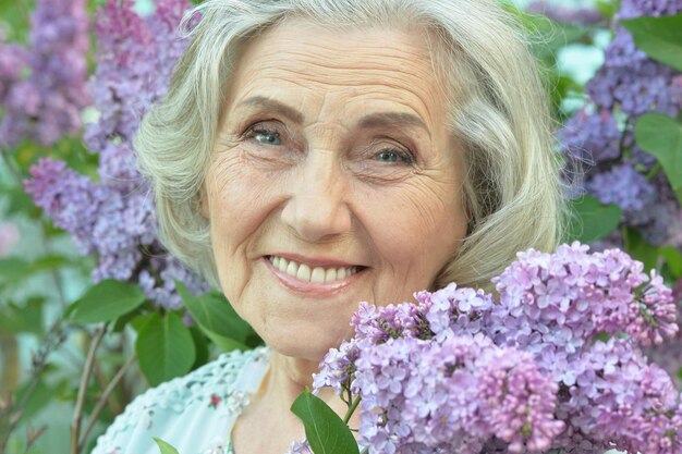 Retrato de mujer hermosa senior feliz con lilas en el parque de primavera