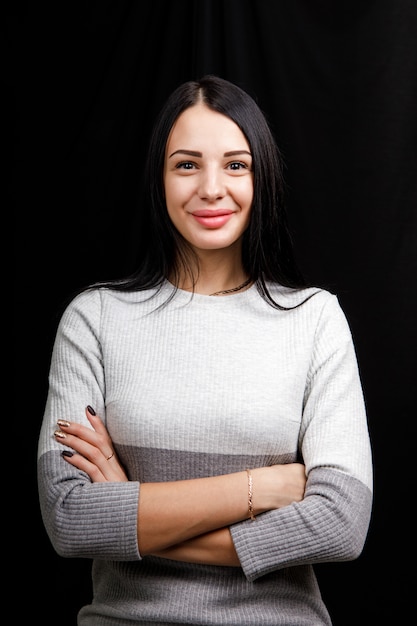 Retrato de mujer hermosa seria con cabello negro, con maquillaje mínimo, mira con calma a la cámara, usa un jersey blanco, se para contra el espacio negro, está sumido en pensamientos.