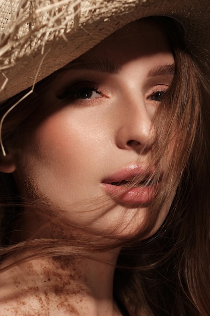 Retrato de una mujer hermosa con un sombrero de paja, cabello suelto y maquillaje desnudo. Rostro de belleza.