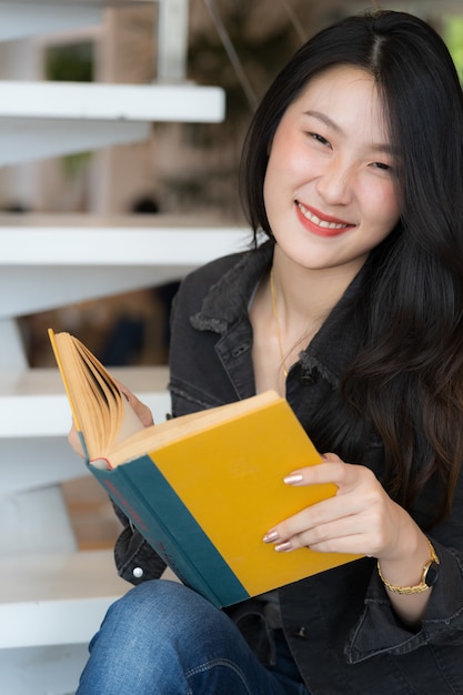 Retrato de mujer hermosa sonriendo mientras lee el libro amarillo en la escalera