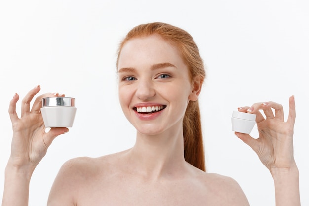 Retrato de mujer hermosa sonriendo mientras toma un poco de crema facial aislado en blanco
