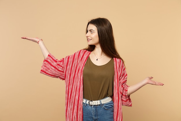 Retrato de mujer hermosa sonriente en ropa casual extendiendo las manos señalando a un lado aislado sobre fondo de pared beige pastel en estudio. Personas sinceras emociones, concepto de estilo de vida. Simulacros de espacio de copia.