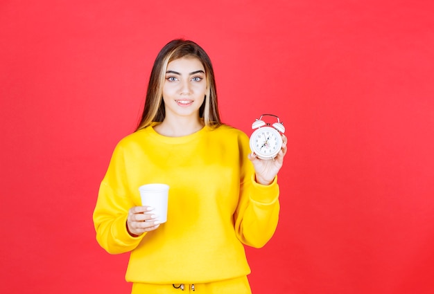 Retrato de mujer hermosa sosteniendo la taza y el reloj en la pared roja