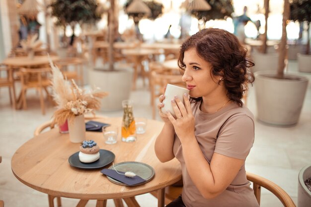 Retrato de una mujer hermosa con una taza de café en sus manos en un café de la ciudad