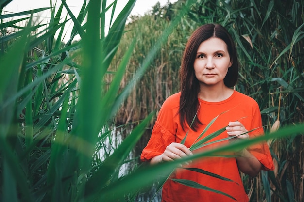 Retrato de una mujer hermosa vestida con ropa roja de pie contra el telón de fondo de las cañas y el lago