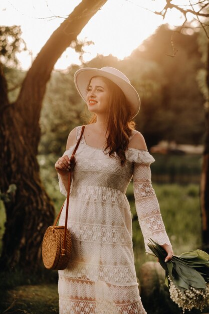 Retrato de una mujer hermosa con un vestido blanco y un sombrero con lirios del valle al atardecer una niña