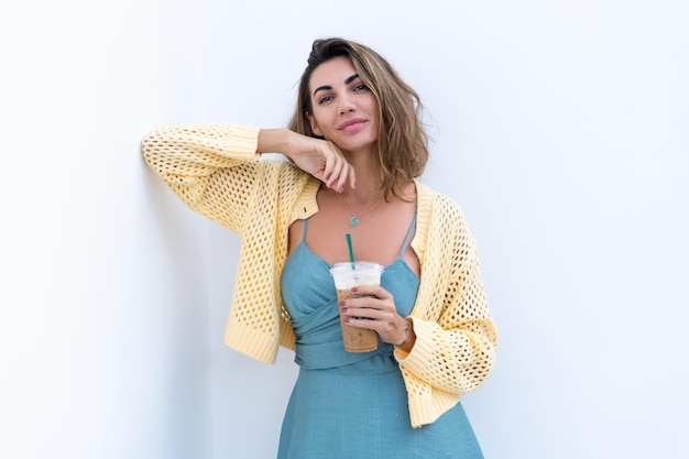 Retrato de mujer hermosa en vestido de verano verde sobre fondo blanco luz natural sosteniendo café helado capuchino feliz sonriendo emocionado