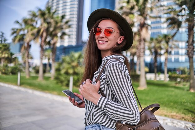 Retrato de mujer hipster despreocupada elegante con sombrero de fieltro y gafas de color rojo brillante