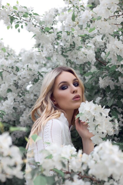 Retrato de una mujer en un huerto de manzanos con un vestido blanco. Rostro de una niña en flores de flores de Apple cerrar