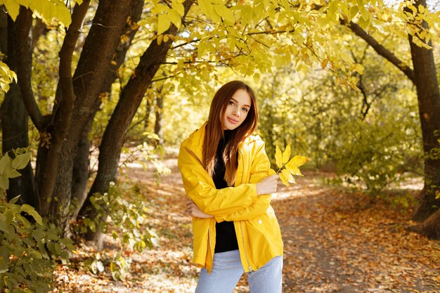 Retrato de mujer con un impermeable amarillo otoñal frente al bosque amarillo otoñal en un paseo. humor otoñal