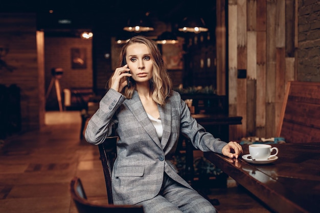 Retrato de una mujer independiente profesional centrada ocupada sentada en un restaurante con una taza de café y hablando por teléfono. Concepto de empleo