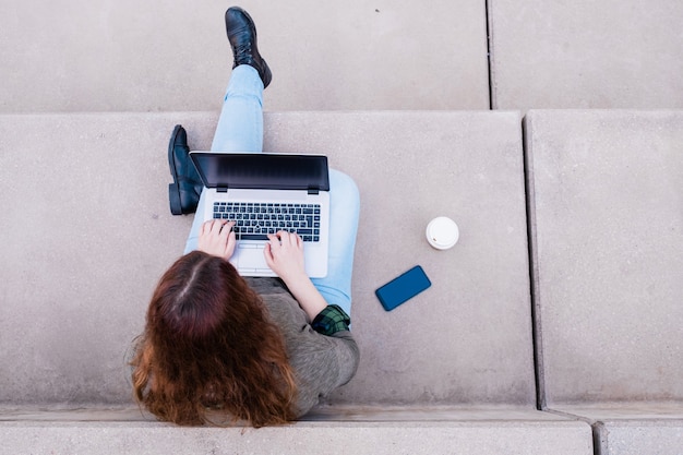 Retrato de mujer independiente usando laptop mientras está sentado en las escaleras en el concepto de Blogger de las calles de la ciudad